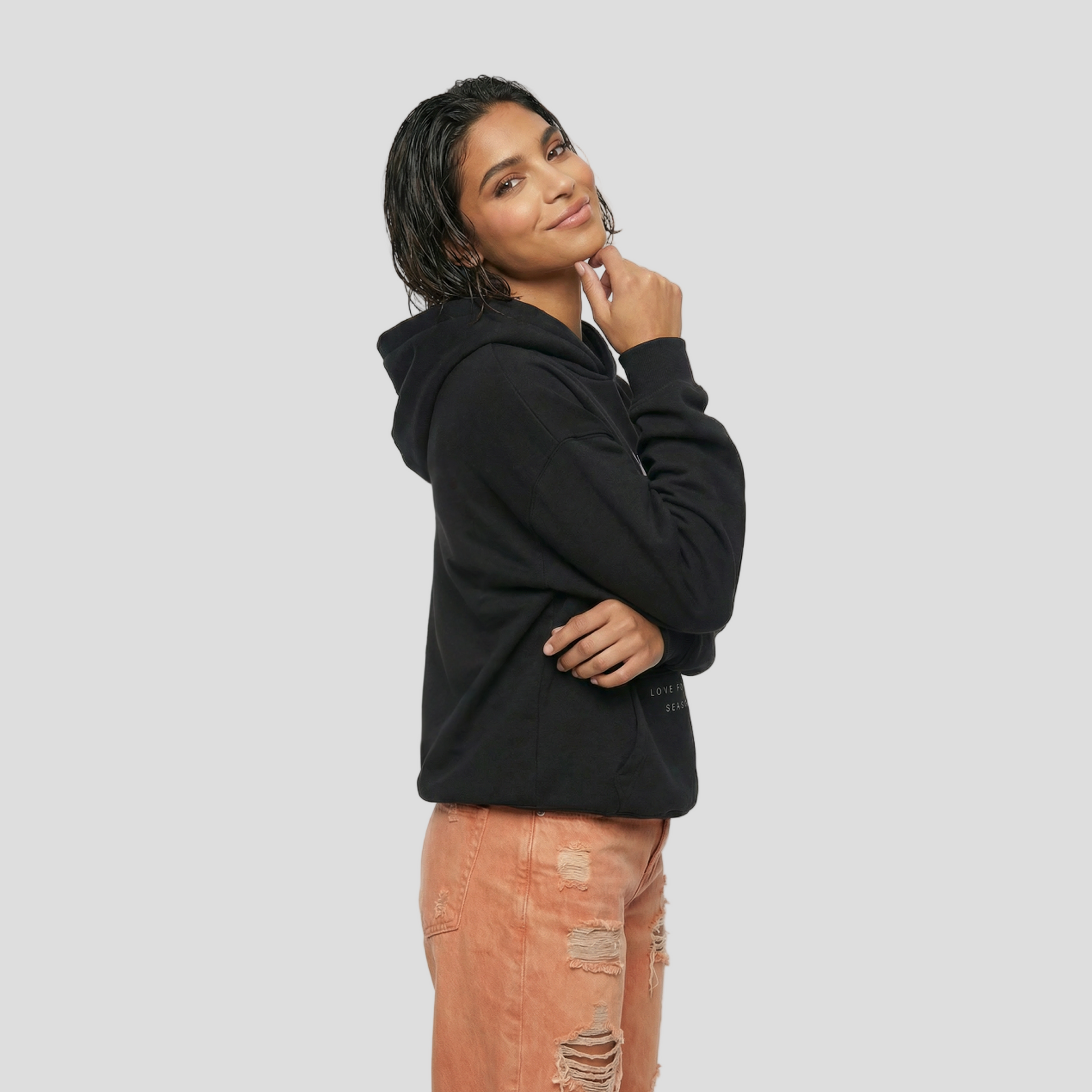 Person wearing a black hoodie and ripped jeans on a white background