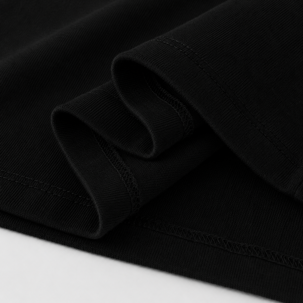 Close-up of folded black fabric with visible ribbed texture and stitching, photographed against a white background.