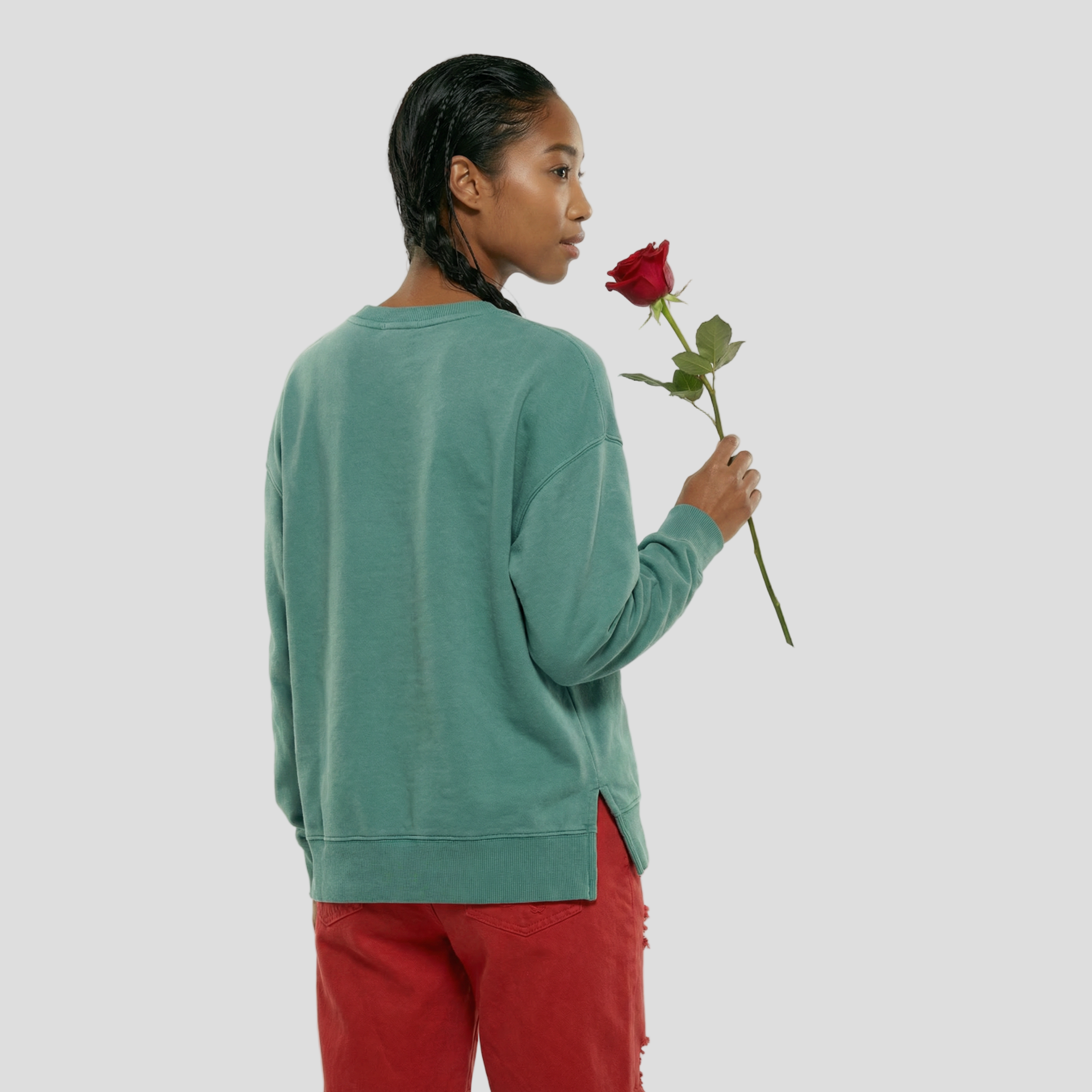 Person wearing a teal sweater and red pants holding a red rose on a white background