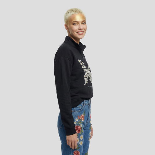 Person wearing a black sweatshirt with a floral design and blue jeans with floral embroidery on a white background