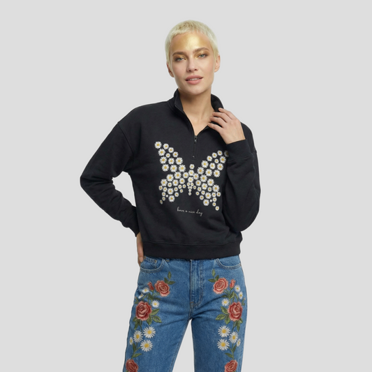 Person wearing a black sweater with a floral butterfly design and blue jeans with floral embroidery on a white background