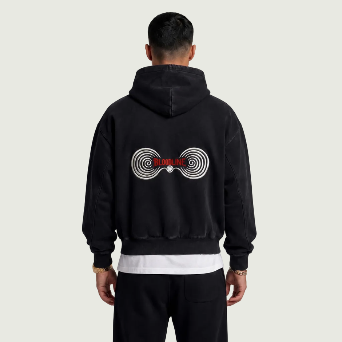 Person wearing a black hoodie with a logo on the back against a gray background