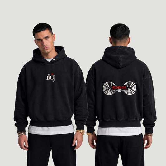 Person wearing a black hoodie with a logo on the front and text on the back, standing against a plain background.